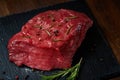 Raw meat beef steaks on black slate board with spices and rosemary over wooden background, copy space Royalty Free Stock Photo