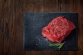 Raw meat beef steaks on black slate board with spices and rosemary over wooden background, copy space Royalty Free Stock Photo