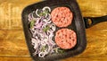 Raw meat burger cutlets, with spices, sliced onion and rosemary sprigs on frying pan Royalty Free Stock Photo