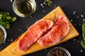 Raw meat on a cutting board. Dark background. Preparation for cooking pork meat. Various spices, seasonings lie nearby