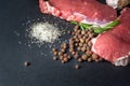 Raw meat and pepper. Close-up of two slices of fresh raw meat and a rosemary branch on a black slate stone plate. Preparing meat Royalty Free Stock Photo