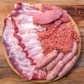 Raw meat products.Barbecue pork ribs, steaks, grilled sausages,minced meat, garnished with spices on a round wooden chopping board Royalty Free Stock Photo