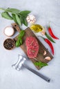 Raw meat. Raw beef steak on a cutting board with with peppers and spices and meat hammer on a gray concrete background Top view. Royalty Free Stock Photo