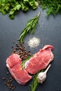 Raw meat salt and spices. Top view of slices of fresh raw meat, garlic, rosemary and spices on a black slate stone plate. Royalty Free Stock Photo