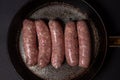 Raw meat sausages in a frying pan on a black background. Royalty Free Stock Photo