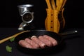 Raw meat sausages in a frying pan on a black background. Royalty Free Stock Photo