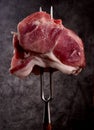 Raw meat stuck on a big fork on a black background