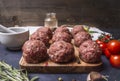 Raw meatballs on a cutting board with vegetables and herbs on wooden rustic background close up