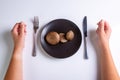 Raw Jersey cow mushroom in a black plate and a knife and fork nearby on a white background top view. Human hands near Royalty Free Stock Photo