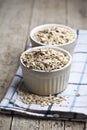 Raw oat flakes in ceramic bowls on linen napkin, golden wheat ears on rustic wooden background Royalty Free Stock Photo