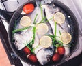 Raw orata fish on frying pan cooking with lemon, tomatoes and greenery. Top view