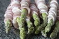 Raw organic asparagus, wrapped in streaky bacon, on a black granite worktop. Fresh seasonal produce concept