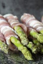 Raw organic asparagus, wrapped in streaky bacon, on a black granite worktop. Fresh seasonal produce concept