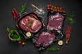 Raw organic marbled beef with spices on a wooden cutting board on a black slate, stone or concrete background Royalty Free Stock Photo