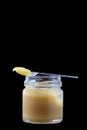 Raw organic royal jelly in a small bottle with litte spoon on black