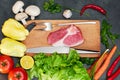 Raw organic vegetables with fresh ingredients for healthy cooking on dark backgroundRaw meat. Raw beef steak on a cutting board wi Royalty Free Stock Photo