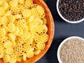 Raw pasta in a bamboo bowl and spice black pepper, cumin jeera on black wooden background