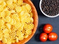 Raw pasta in a bamboo bowl and spice black pepper, small tomato on black wooden background Royalty Free Stock Photo