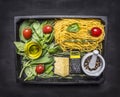 Raw pasta with basil, cherry tomatoes, butter, cheese grater and cheese, whole pepper in a mortar wooden box on wooden rustic Royalty Free Stock Photo