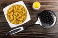 Raw pasta in white bowl, salt shaker, skimmer on wooden table. Top view