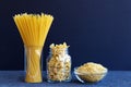 Raw pasta. Glass jar filled with various spaghetti, farfalle, noodles on dark blue background Royalty Free Stock Photo