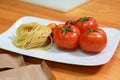 Raw pasta noodles with fresh tomatoes on a white plate. Fresh spaghetti ingredients on the wooden table Royalty Free Stock Photo