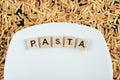 Raw pasta scattered around white plate with wooden letters