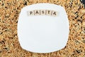 Raw pasta scattered around white plate with wooden letters