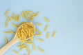 Raw pasta in the wooden spoon on blue background.