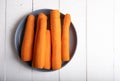 Raw peeled carrots on a blue plate on a white wooden background