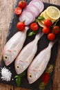 Raw pink dorado or gilt-head sea bream fish with spices, vegetables and lemon close-up on a slate board. Vertical top view Royalty Free Stock Photo