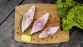 Raw Pomfret fish slices on cutting board on top of wooden table