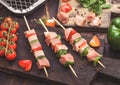 Raw pork and chicken kebab with paprika on chopping board with fresh vegetables and disposable charcoal grill on wooden background Royalty Free Stock Photo