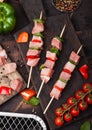 Raw pork and chicken kebab with paprika on chopping board with fresh vegetables and disposable charcoal grill on wooden background Royalty Free Stock Photo