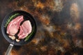 Raw Pork Loin chops on a bone in a black frying grill pan on a old rustic dark metall surface rosemary garlic peppercorns top view Royalty Free Stock Photo