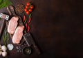 Raw pork loin chops on old chopping board with salt and pepper and vintage meat hatchets and hammer on rusty background.Red pepper