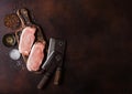 Raw pork loin chops on old vintage chopping board with knife and fork on rusty background. Salt and pepper with fresh rosemary and Royalty Free Stock Photo