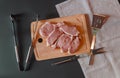 Raw pork meat. Fresh steaks on cutting board on dark surface with kitchen tongs, fork for meat and spatula Royalty Free Stock Photo