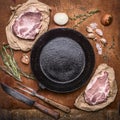 Raw pork meat with ingredients for cooking around cast-iron frying pan with knife for meat meat fork on rustic wooden backgrou Royalty Free Stock Photo