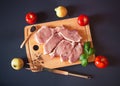 Raw pork meat steaks with fresh vegetables on cutting board on dark background Royalty Free Stock Photo