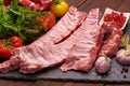 Raw pork ribs on a slate stone plate with spices, colorful tomatoes and red currant on a wooden rustic background