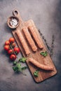 Raw pork sausages with cherry tomatoes and spices on a cutting board, rustic background. Top view, flat lay Royalty Free Stock Photo