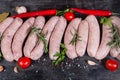 Raw pork sausages among spices and vegetables on dark surface Royalty Free Stock Photo