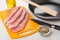 Raw pork schnitzel on cutting board, oil, frying pan, knife