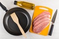 Raw pork schnitzel on cutting board, oil, frying pan, spatula