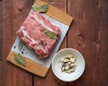 Raw pork in specials and a plate with chopped garlic and ground pepper stand on a wooden table