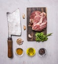 Raw pork steak on a cutting board and vintage meat cleaver with spices, garlic and herbs on wooden rustic background top view clos