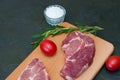 Raw pork steak, rosemary, tomatoes and salt on wooden cutting board, dark background, top view and side view Royalty Free Stock Photo