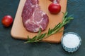 Raw pork steak, rosemary, tomatoes and salt on wooden cutting board, dark background, top view and side view Royalty Free Stock Photo