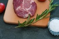 Raw pork steak, rosemary, tomatoes and salt on wooden cutting board, dark background, top view and side view Royalty Free Stock Photo